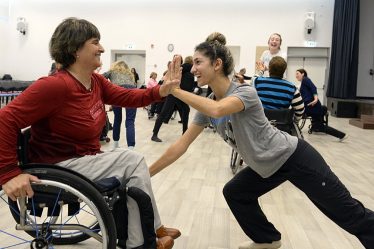 Deux danseuses souriantes se tapant dans la main, l’une en fauteuil roulant, en cours de danse