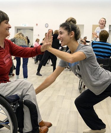 Deux danseuses souriantes se tapant dans la main, l’une en fauteuil roulant, en cours de danse