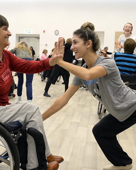 Deux danseuses souriantes se tapant dans la main, l’une en fauteuil roulant, en cours de danse