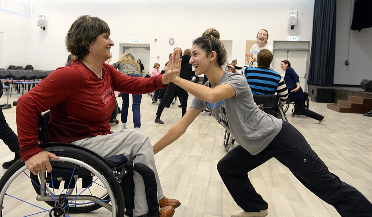 Deux danseuses souriantes se tapant dans la main, l’une en fauteuil roulant, en cours de danse